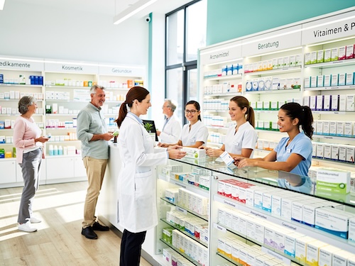 Foto eines modernen deutschen Apotheken-Innenraums. Freundliches Apothekenpersonal (Apotheker:innen, PTA, PKA) berät Kund:innen in einem hellen, einladenden Ambiente. Natürliches Licht und eine Farbgebung aus Weiß-, Blau- und Grüntönen.