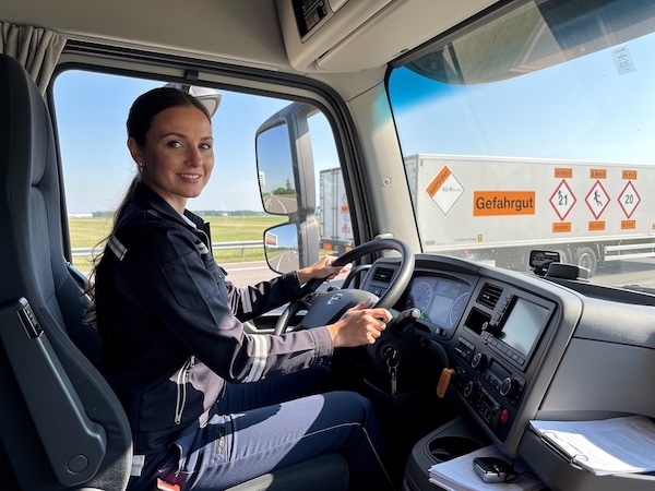 Attraktive, selbstbewusste LKW-Fahrerin in einem LKW für Gefahrguttransporte, professionell und stylisch gekleidet, am Steuer sitzend.